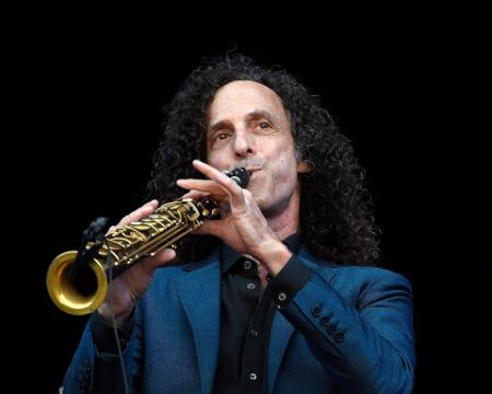 Kenny G in a blue suit playing a saxophone.